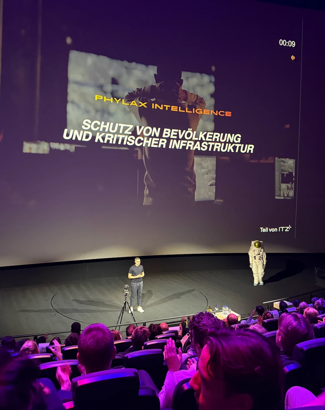 The Phylax Intelligence pitch at the *zünder Award 2026 final in the Verkehrshaus der Schweiz, Lucerne, with the slide "Schutz von Bevölkerung und kritischer Infrastruktur" on the big screen