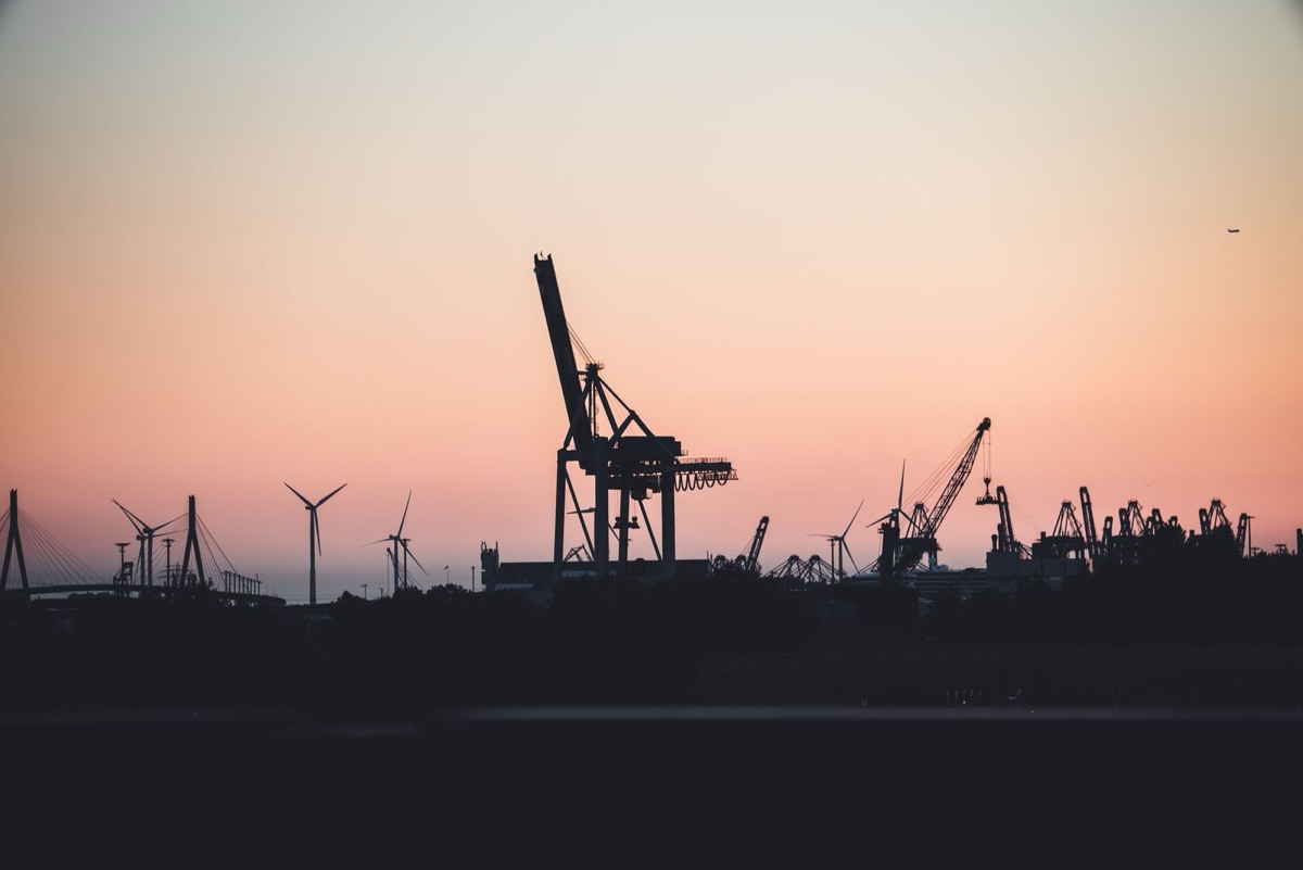 Silhouettes of port cranes and wind turbines at sunset